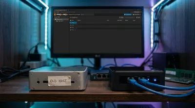 Mini PC BMAX antiguo etiquetado 'OLD HOST' junto al nuevo GMKtec G11 con doble conexión de red, sobre una estantería de homelab con iluminación RGB y un monitor mostrando el panel de Proxmox de fondo.