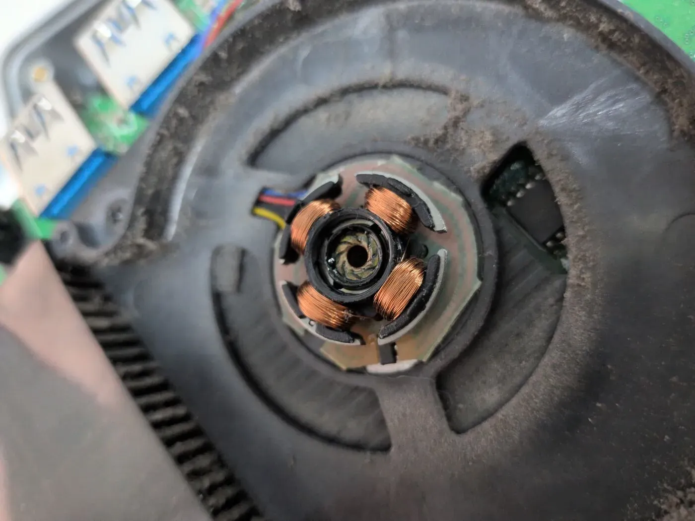 El culpable del ruido, al descubierto Rotor de un ventilador desmontado, mostrando las cuatro bobinas de cobre del estátor y el eje central sucio de polvo
