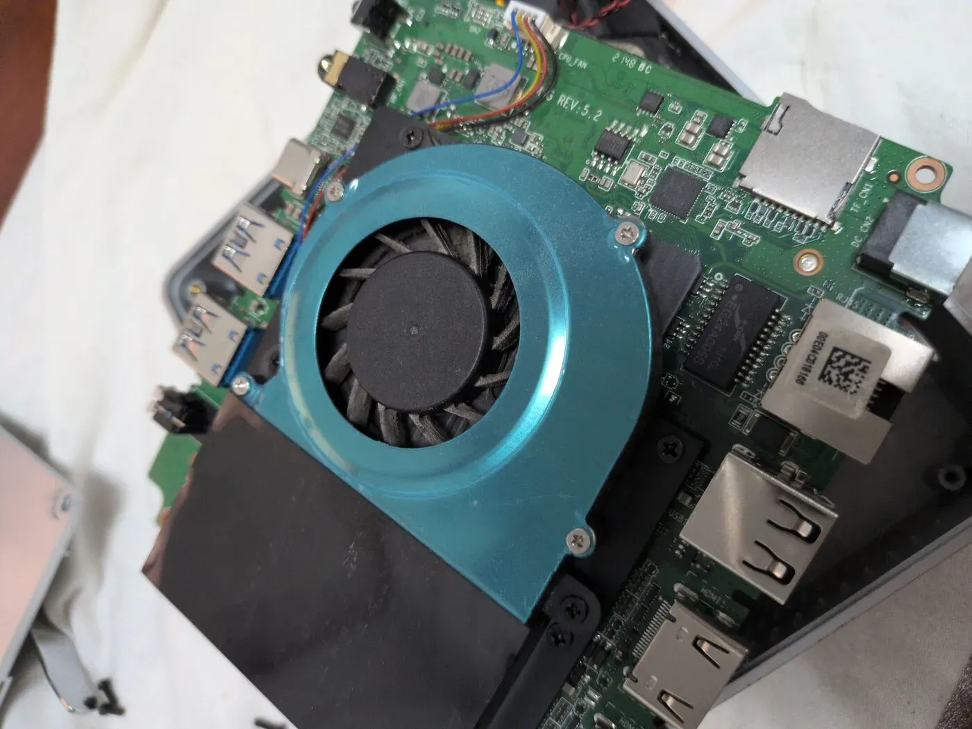 El ventilador, atrapado tras los puertos Ventilador blower centrífugo atornillado a la parte trasera de la placa base de un mini PC, junto a los puertos USB