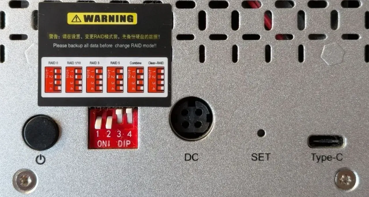 La misma carcasa después del cambio: los interruptores 1 y 2 están hacia abajo, en ON, y el 3 y el 4 hacia arriba, en OFF. La etiqueta de advertencia, el conector DC, el botón SET y el puerto USB-C se ven igual que en la foto anterior.